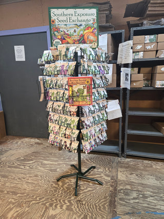 A retail display wire spinner rack with a sign reading 'Southern Exposure Seed Exchange', featuring various colorful seed packets for plants like flowers herbs and vegetables.